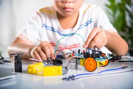 Asian kid boy plugging energy and signal cable to sensor chip with Arduino robot car
