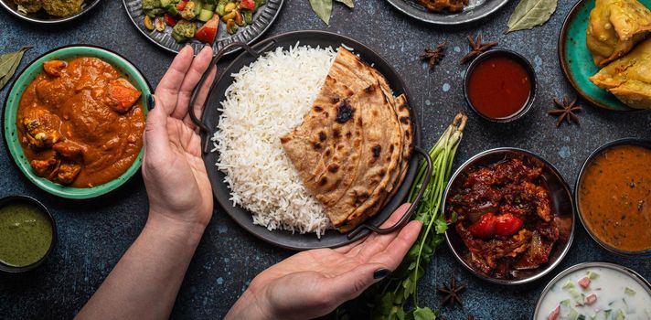 Female hands serving Indian ethnic food buffet on rustic concrete table