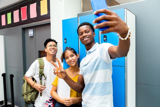 Happy group of teen multiracial classmate take a selfie in high school corridor next to lockers.