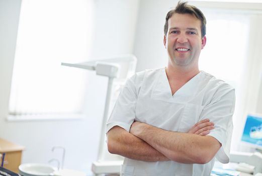 Your teeth look great. Portrait of a male dentist standing by the dental equipment in his office