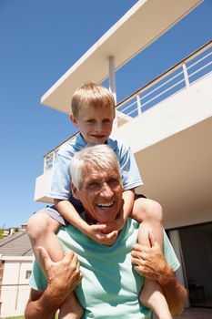 Im still fit enough to give piggyback rides. a grandfather giving his grandson a piggyback ride outdoors.