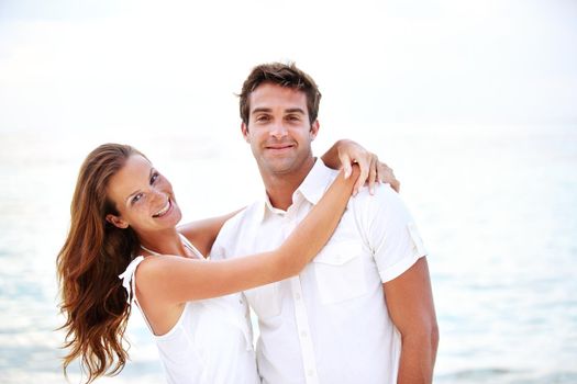 Honeymoon happiness. A beautiful young woman embracing her handsome man against a scenic ocean background.