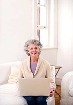 Connecting with her old-time friends. a senior woman sitting with a laptop on a sofa.