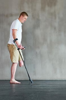 Stepping out. an young man with one leg walking on crutches in a gym.