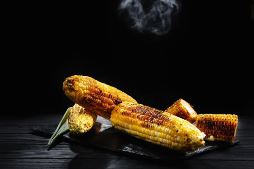 Grilled corn with smoke. A cob of corn roasted over charcoal on a wooden board. Whole corn cobs.