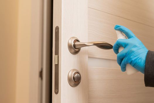 Caucasian woman in gloves disinfecting the door handle.