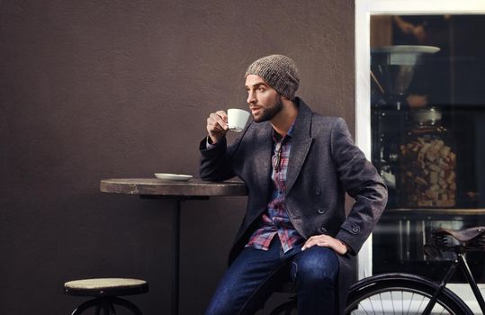 Sidewalk sipping. a handsome young man in winter wear having a beverage at a sidewalk cafe.