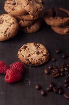 Chocolate chips cookies with red raspberries and coffee beans on dark old wooden table.