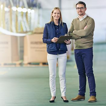 Running a factory with finesse. Portrait of a two smiling managers standing on the warehouse floor.
