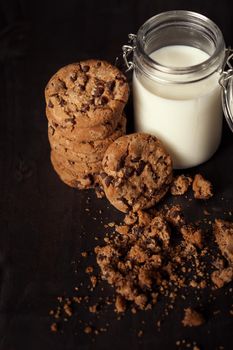 Homemade chocolate chip cookies with bottle of milk and crumbs on rustic wooden table.