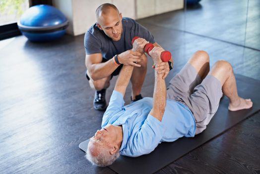 Guiding him back to wellness. a physiotherapist helping a senior man with weights.