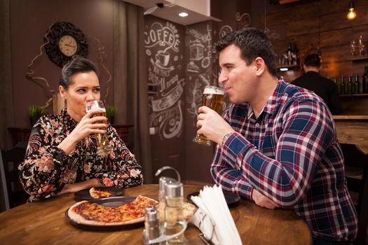 Happy couple drinking beer and eating pizza.