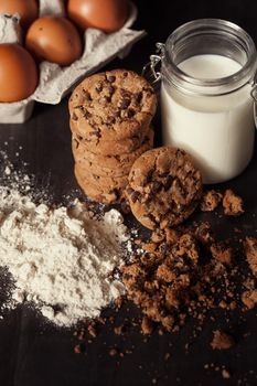 Homemade chocolate chip cookies with bottle of milk, white flour and crumbs
