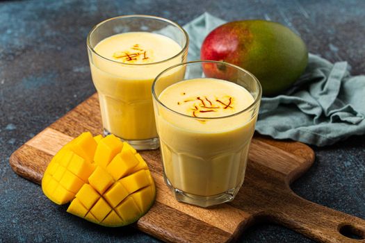 Drink mango lassi in two glasses on rustic concrete table with fresh ripe cut manfo from above