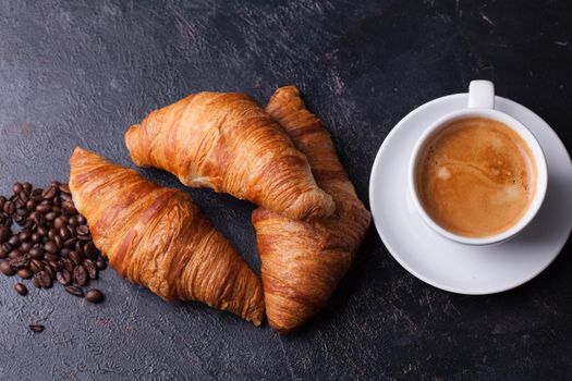 Croissants with cup of coffee and coffee beans on dark wooden table