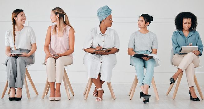 Diversity, interview and business people in waiting room at a job, hiring or recruitment center. Corporate, women and professionals talking with technology in a unemployment office for a work vacancy