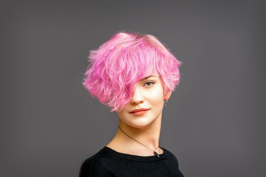Portrait of beautiful young white woman with a pink short hairstyle on dark background with copy space.