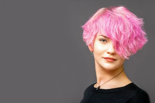 Portrait of beautiful young white woman with a pink short hairstyle on dark background with copy space.