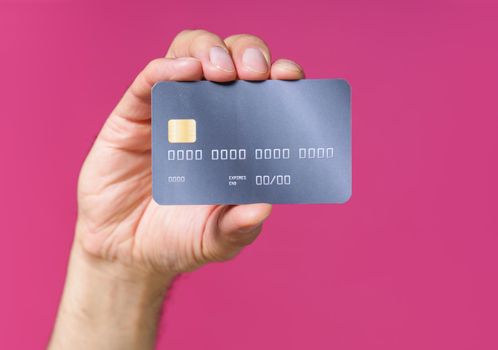 Best offer, dark grey-purple debit, credit card in man hand isolated on pink background. Financial, banking concept. No face visible