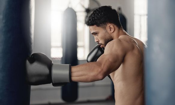 Training, fitness and workout man boxer, sweating and doing a cardio exercise at the gym. Sporty, sweaty and determined male athlete punching a bag at a sports boxing center for health and wellness