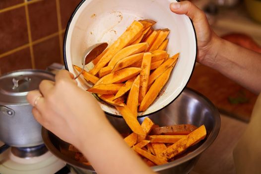Selective focus on wedges of organic sweet potato in an enamel bowl in the hands of a cook preparing healthy vegan meal