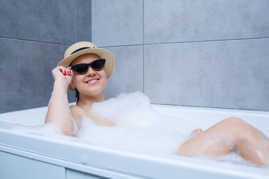 Young woman in a hat and sunglasses takes a bath at home. Relax after a hard day. The spa is a relaxing procedure.