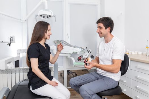 Dentist holding dental articulator with dental gypsum prosthesis model showing it to a patient