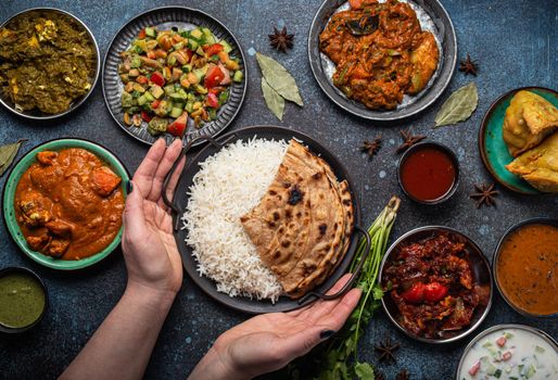 Female hands serving Indian ethnic food buffet on rustic concrete table