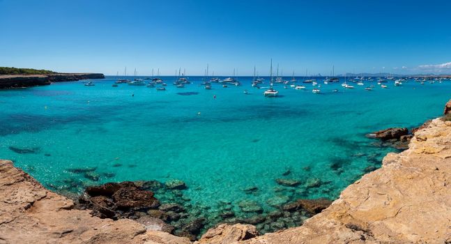 Panoramic view of Cala Saona with sailboats anchored in the Mediterranean Sea