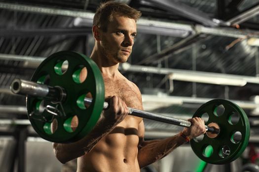 Handsome young fitness man working out with a barbell at the gym