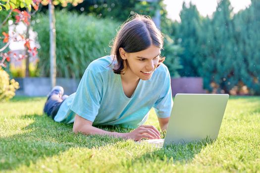 Teenage male lying on the grass using a laptop