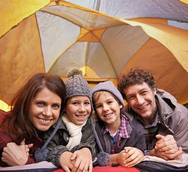 Family camping is family bonding. Portrait of smiling family of four relaxing in tent on a camping holiday.