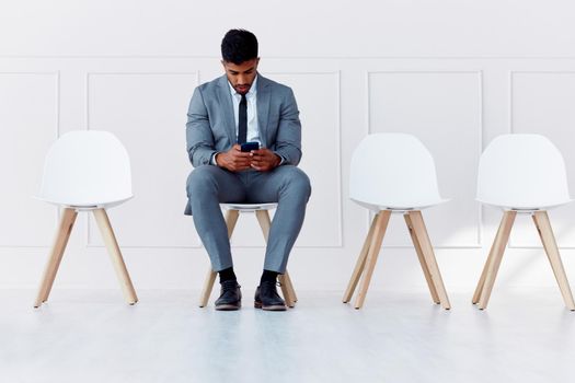 Human resources, recruitment and man on chair with phone in empty corporate office waiting room. Professional company interview for candidate and rejection in the job career hiring process.