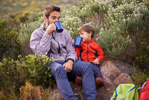 Lets take a load off. a happy father and son having something to drink while on a hike together.