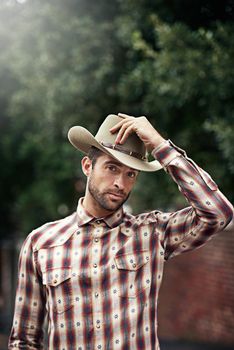 Out west its all about how you wear your attitude. a handsome cowboy wearing a check shirt and stetson.