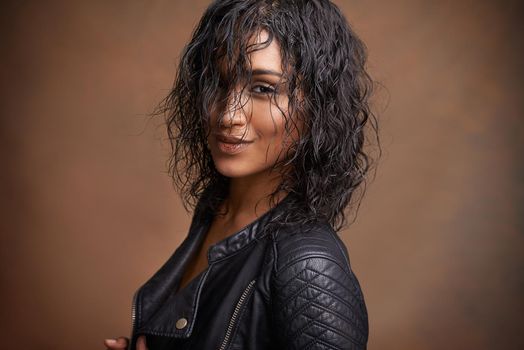 Leather style. Studio shot of an attractive young woman in a leather jacket against a brown background.