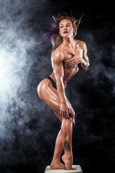 Muscular young fitness sports woman with strong fit body on black background.