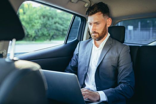 Male businessman working on laptop sitting on passenger seat of car