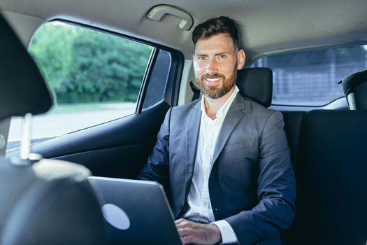 Male businessman working on laptop sitting on passenger seat of car