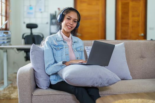 Portrait of an African American sitting on the sofa wearing on-ear headphones and using a computer at home