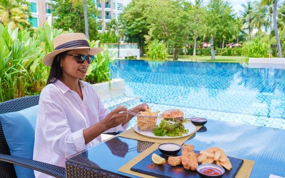Asian women having lunch by the pool with hamburger and fish and chips