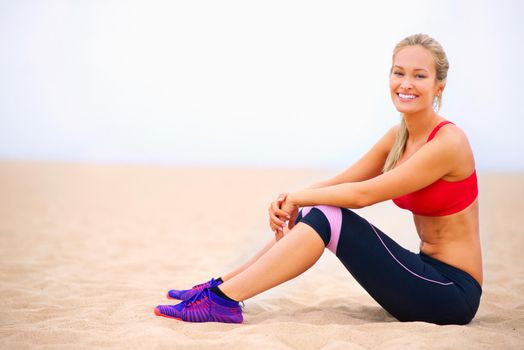 Feeling every bit as great as I look. Portrait of a young woman in sportswear sitting on the beach.