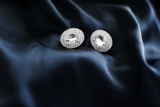 Luxury diamond earrings on dark blue silk background, holiday glamour jewelery present