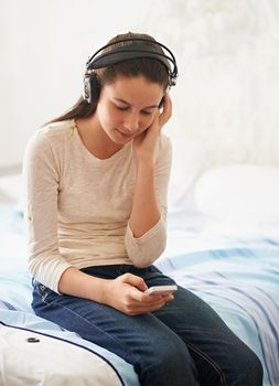 Lost in a world of music. a teenage girl sitting on her bed and listening to music.
