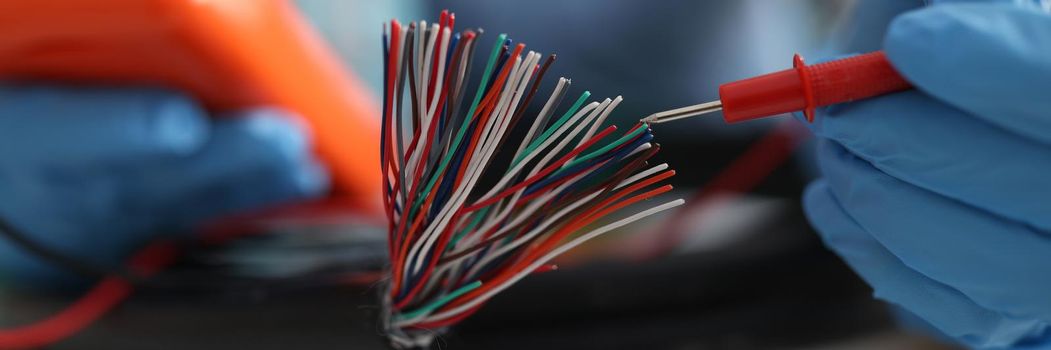 Master repairman testing multicolored wires from cable using tester closeup