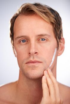 Moisturiser, the modern mans warpaint. Portrait of a handsome man focusing on applying moisturiser.