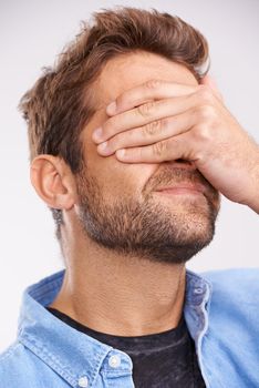 Facepalm. Studio shot of a handsome young man covering his eyes in regret against a gray background.