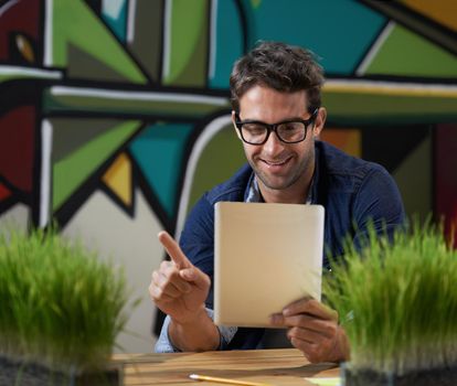 A handsome designer in his natural habitat. a male entrepreneur using a digital tablet at his desk.