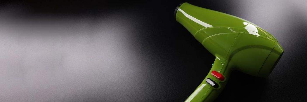 Closeup of green professional hair dryer against dark background