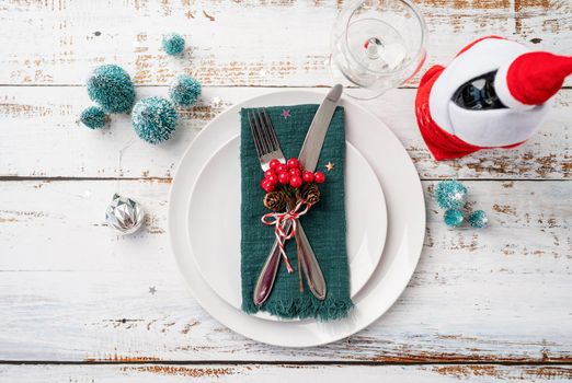 Christmas table setting with white dishware, silverware and red and green decorations on white wooden background. Top view.